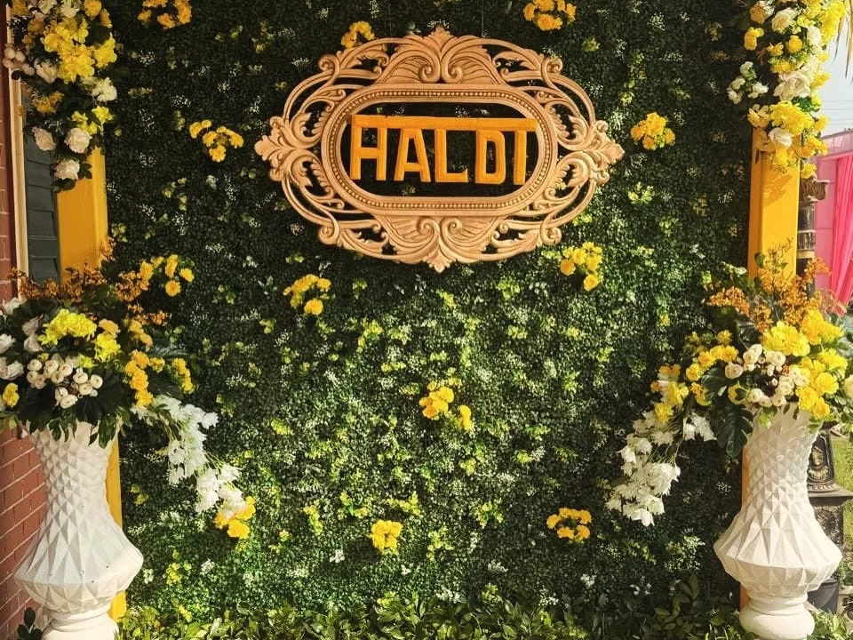 Green floral wall with a Haldi sign, yellow flowers and white vases