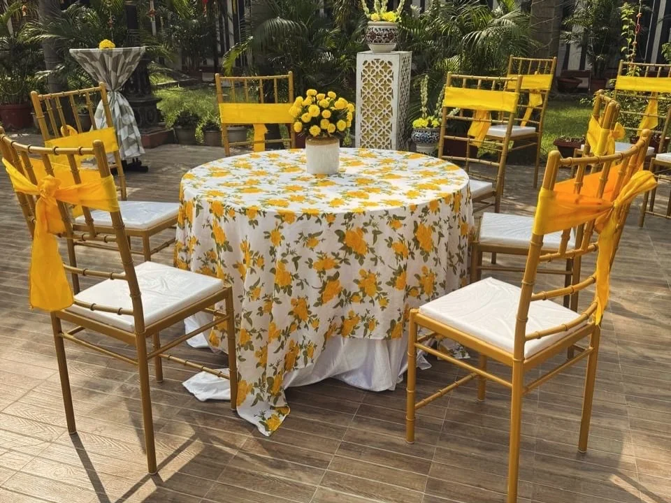 Floral table linen and yellow-accented chairs at a haldi celebration